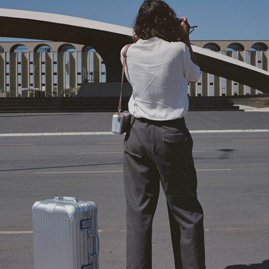 Woman standing next to Rimowa suitcase by road